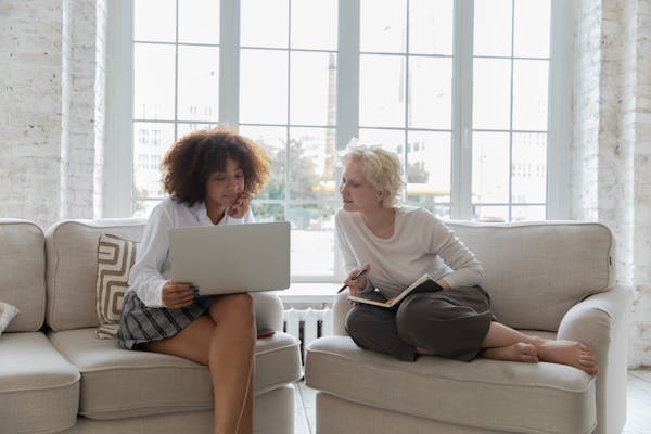 Positive young diverse girlfriends working on project together using laptop in apartment